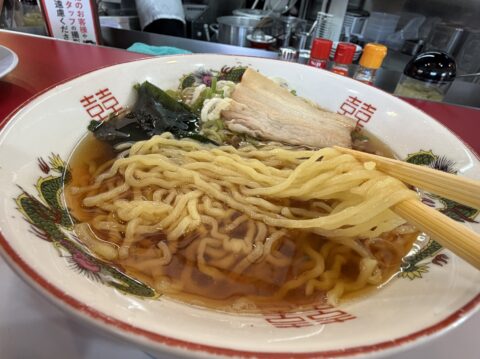 箸で持ち上げた朝ラーの麺。あっさり醤油スープに昔ながらの縮れ麺