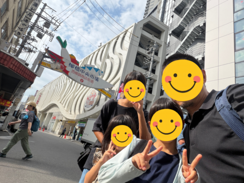 柳橋中央市場の看板前で記念撮影する三姉妹とお父さん