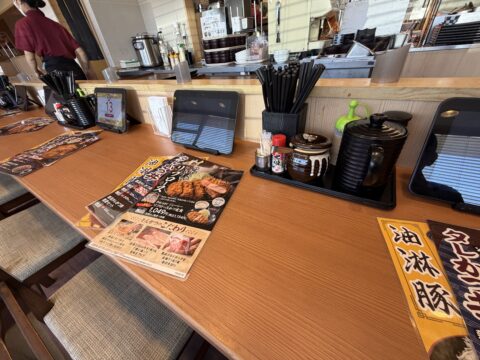 とんから亭の店内カウンター席。タッチパネル端末と卓上メニュー、調味料が並ぶ