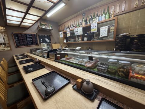 桜鮨の店内。ネタケースのあるカウンター席と一升瓶が並ぶ棚