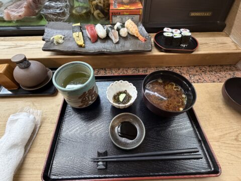 桜鮨のにぎり定食。お茶と小鉢、赤出汁が並び、亭主が下駄板に寿司を並べている途中
