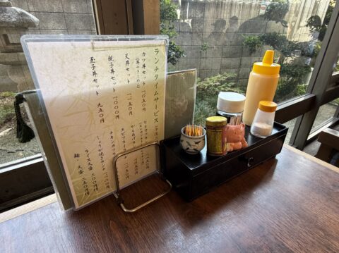 きしめん竹亭の窓際席。窓の外に中庭が見え、卓上には調味料とメニューが並ぶ