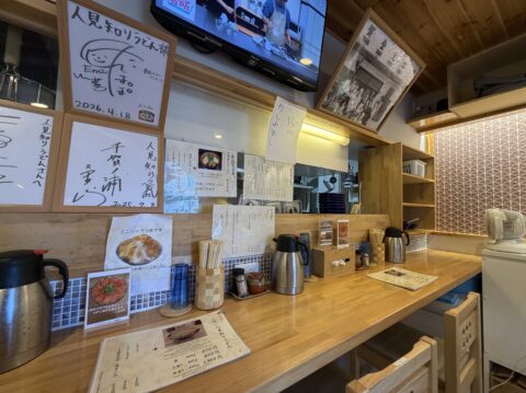 人見知りうどんの店内。カウンター席と壁に飾られた色紙や写真パネル