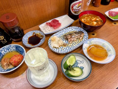食べ残しが集まった魚源食堂のテーブル。鯖、揚げ物、冬瓜、漬物と瓶ビール
