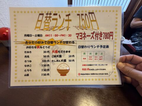 日替ランチ750円の案内。お好きな具のトッピング価格と日替わり予定表