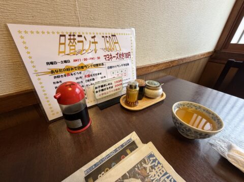 卓上の日替ランチ750円のPOP、スポーツ新聞と湯呑み