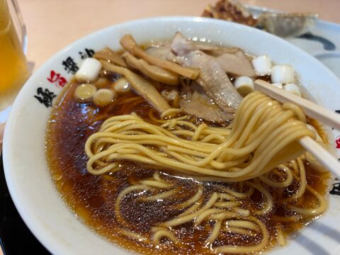 濃厚ブラックの麺を箸で持ち上げたところ。黒い醤油スープに白ねぎのぶつ切りとメンマ