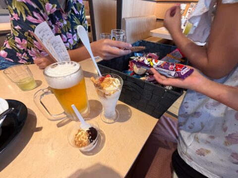完食した子供がお菓子のカゴから選んでいるところ。テーブルにはビールとミニパフェ、ミニアイス