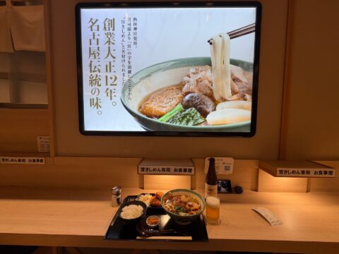 「創業大正12年。名古屋伝統の味。」のパネルと、宮きしめん専用お食事席の飛騨牛コロッケ定食と瓶ビール