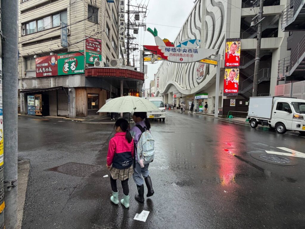 雨の柳橋中央市場の入口（西柳錦商店街）を傘をさして歩く子どもたち